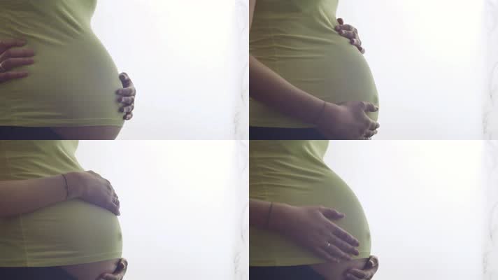 孕妇轻抚摸怀孕肚子站在窗口实拍特写