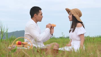 阳光明媚夏日夫妇坐在草地上分享牛角面包